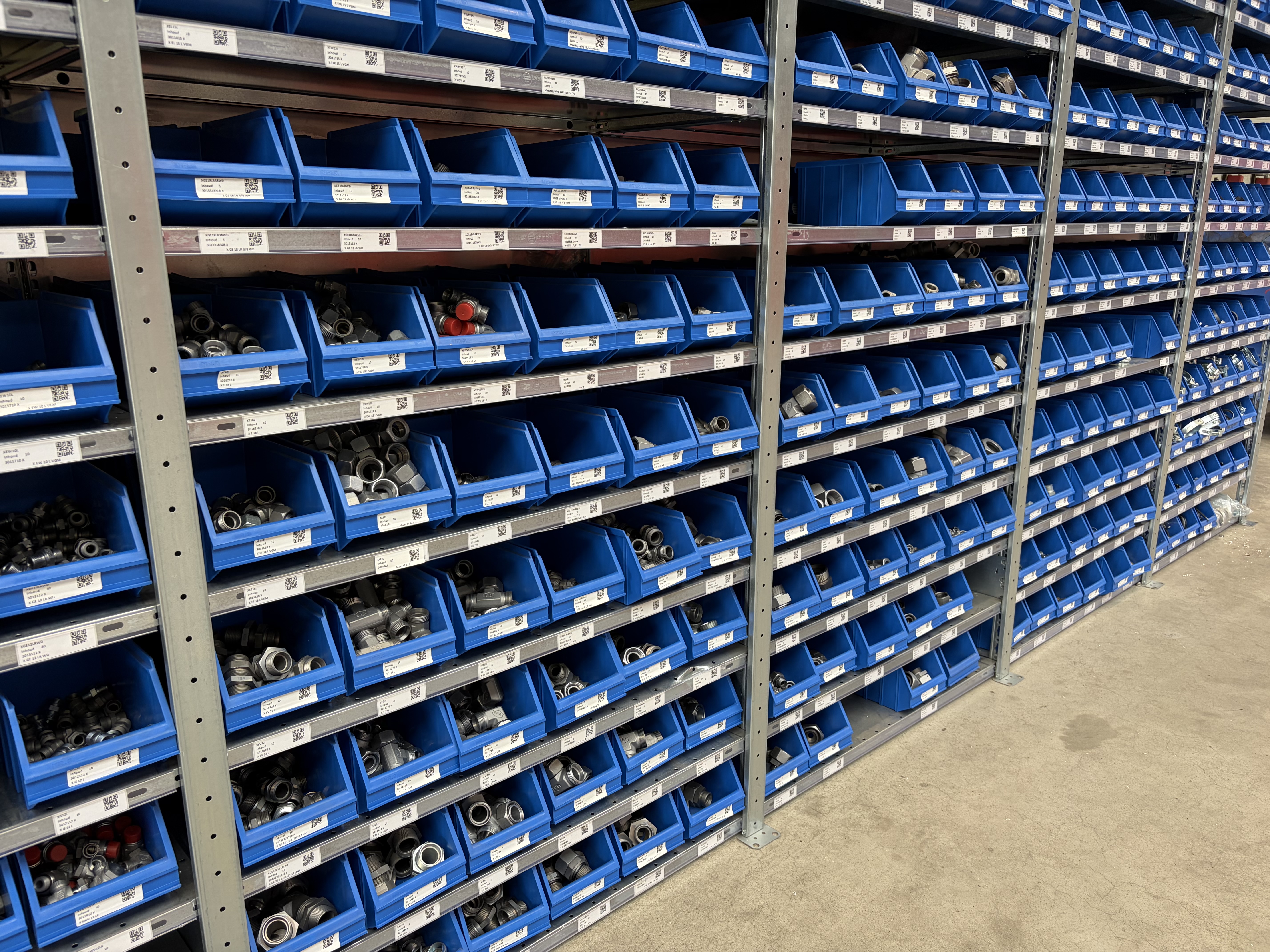 Stelling met blauwe 2-bin-voorraadbakken en scanbare artikellabels voor technische koppelingen